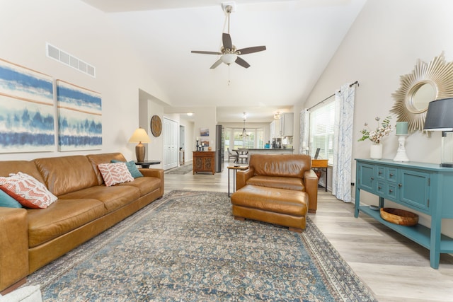 living room with ceiling fan, light wood-style floors, high vaulted ceiling, and a chandelier