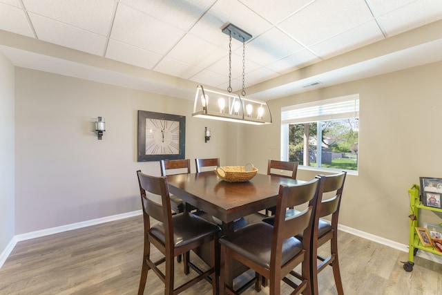 dining space with a drop ceiling, light wood-style flooring, and baseboards