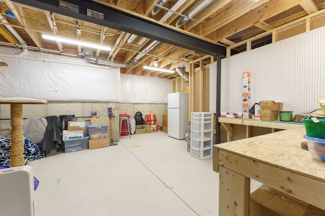 unfinished below grade area featuring freestanding refrigerator and a workshop area