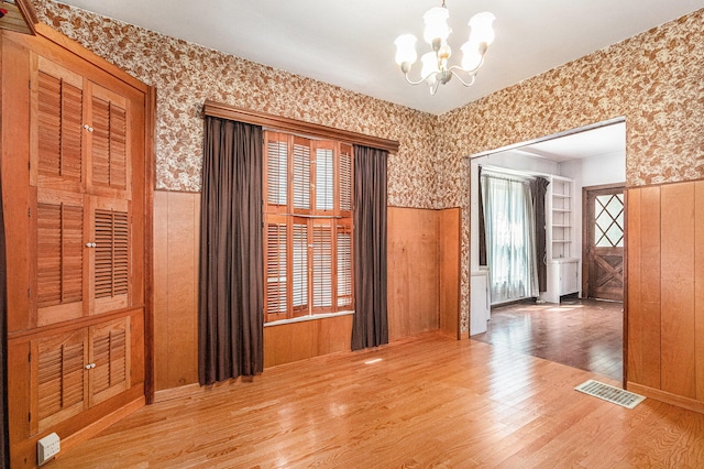 unfurnished room featuring visible vents, wainscoting, wood finished floors, a notable chandelier, and wallpapered walls