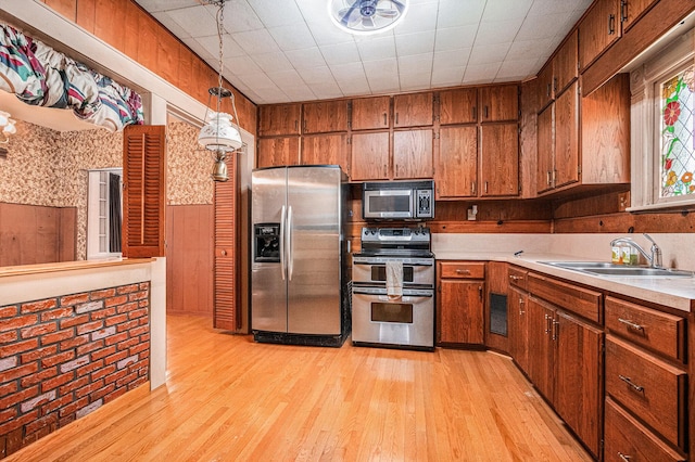 kitchen with a sink, light wood finished floors, light countertops, brown cabinetry, and stainless steel appliances