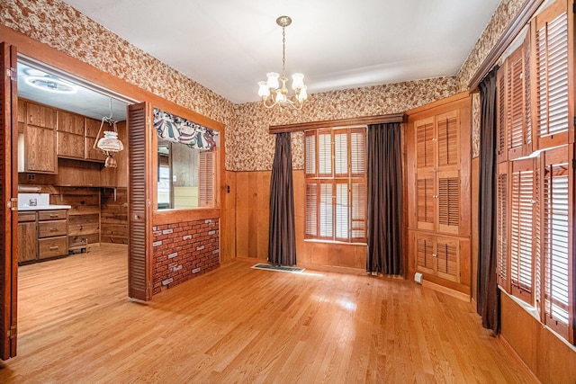 unfurnished dining area featuring wooden walls, an inviting chandelier, wainscoting, light wood-style floors, and visible vents