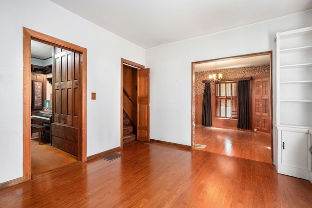 empty room featuring visible vents, wood finished floors, stairway, baseboards, and a notable chandelier