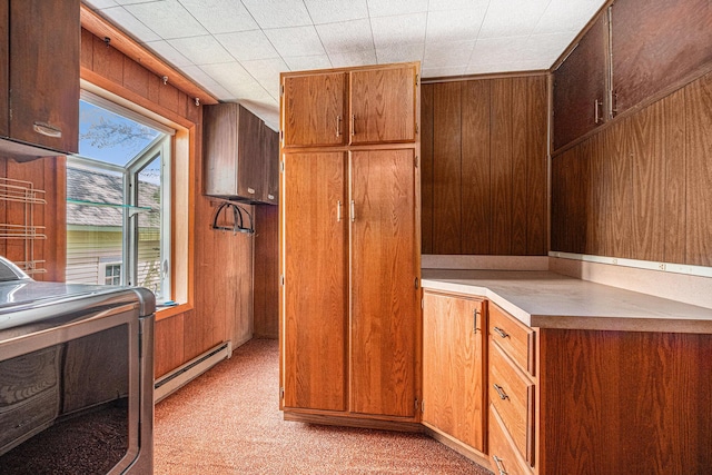 kitchen featuring light colored carpet, wood walls, washer / dryer, and a baseboard radiator