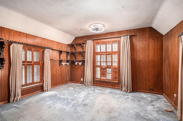 spare room featuring wooden walls, carpet, and lofted ceiling