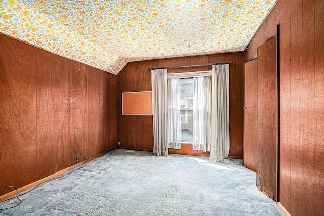 unfurnished bedroom with carpet floors, vaulted ceiling, and wood walls