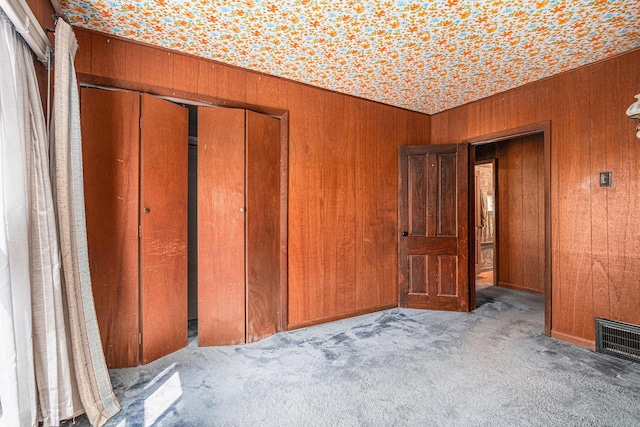 unfurnished bedroom featuring wooden walls, a closet, carpet flooring, and visible vents