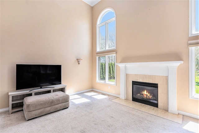living area with a tiled fireplace, carpet, and a towering ceiling