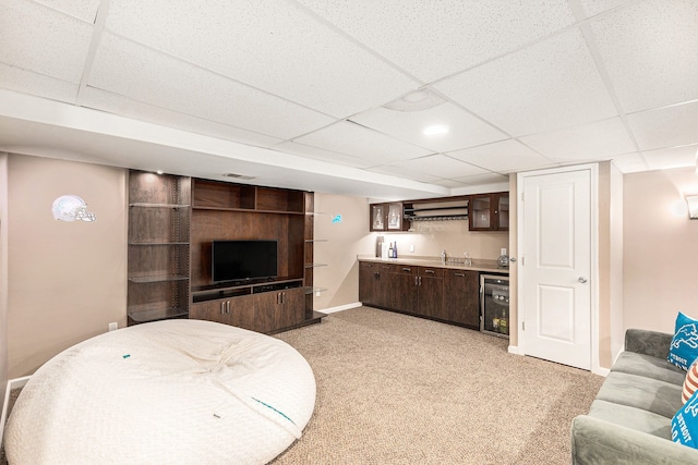 living area with light carpet, beverage cooler, wet bar, baseboards, and a drop ceiling