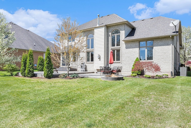 back of house with roof with shingles, central AC unit, brick siding, a yard, and a patio