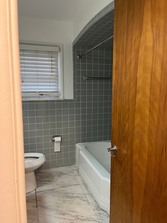 bathroom featuring marble finish floor, shower / bathtub combination, toilet, and tile walls
