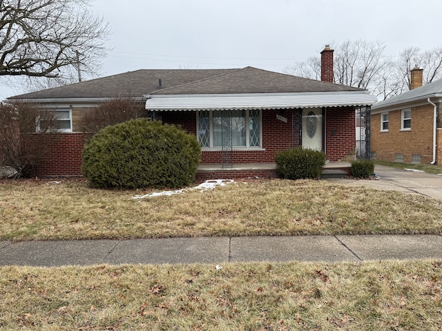 view of front of home featuring covered porch, a chimney, brick siding, a front lawn, and a shingled roof