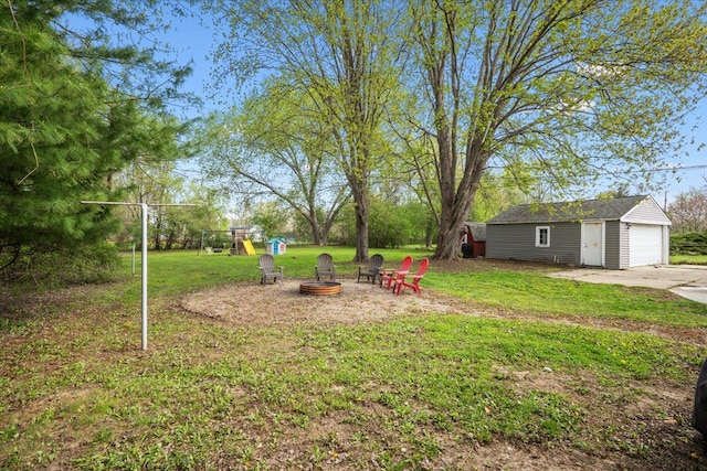 view of yard featuring a detached garage, an outbuilding, a fire pit, and a playground