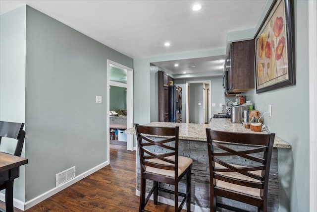 kitchen featuring visible vents, light stone countertops, fridge with ice dispenser, recessed lighting, and dark wood-type flooring