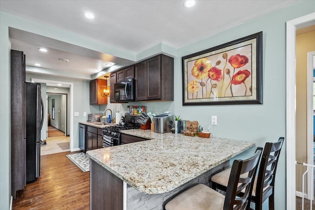 kitchen with appliances with stainless steel finishes, a sink, dark wood finished floors, a peninsula, and recessed lighting