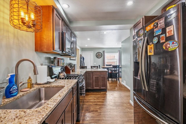 kitchen featuring black range with gas cooktop, a sink, stainless steel microwave, refrigerator with ice dispenser, and dark wood-type flooring