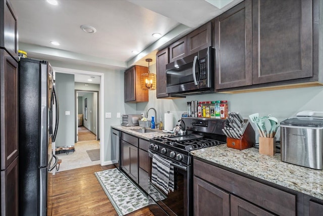 kitchen with light stone countertops, dark brown cabinets, a sink, stainless steel appliances, and light wood-style flooring