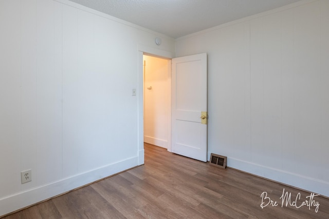 empty room with visible vents, baseboards, crown molding, and wood finished floors