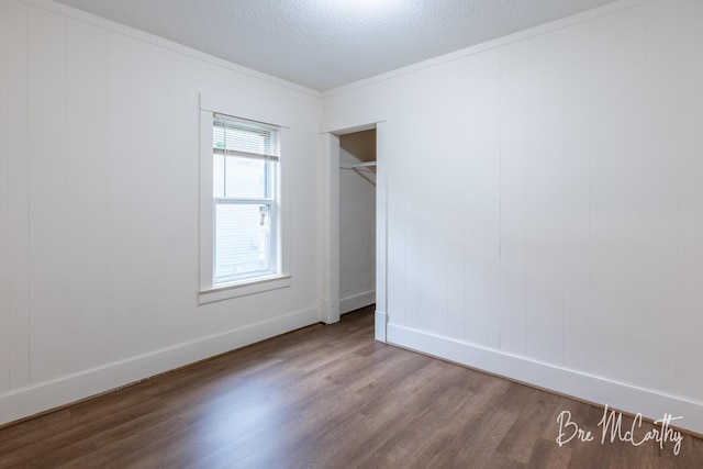 unfurnished bedroom with crown molding, a textured ceiling, baseboards, wood finished floors, and a closet