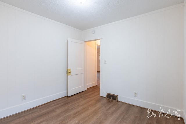 unfurnished room with a textured ceiling, visible vents, crown molding, wood finished floors, and baseboards