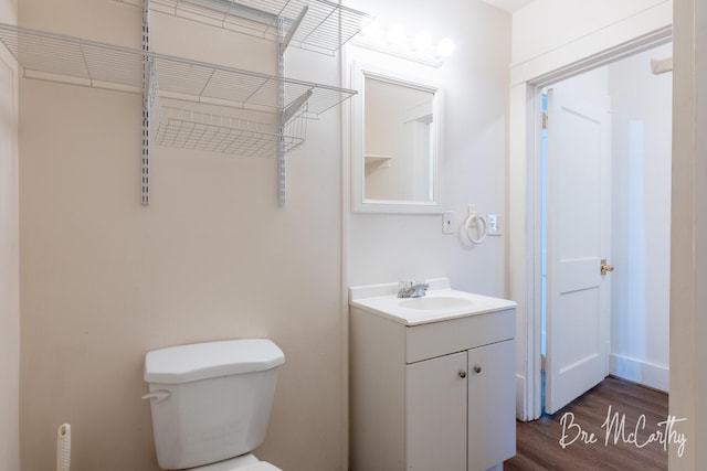 half bathroom with vanity, wood finished floors, and toilet
