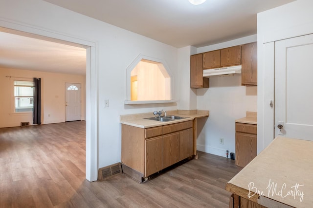 kitchen featuring brown cabinetry, visible vents, wood finished floors, a sink, and under cabinet range hood