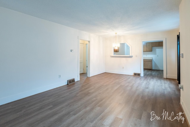 unfurnished living room featuring visible vents, dark wood-style flooring, baseboards, and a chandelier