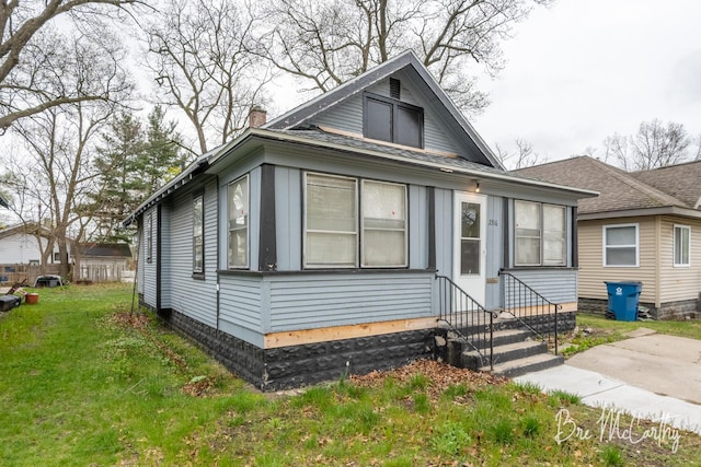 bungalow featuring roof with shingles, a front yard, a chimney, and entry steps