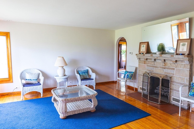 living room featuring a stone fireplace, arched walkways, baseboards, and wood finished floors