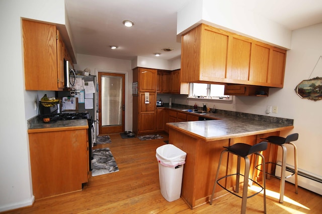 53240 Hemlock Lake Rd, Marcellus, MI 49067 - kitchen featuring dark countertops, light wood-style floors, a breakfast bar area, range with gas stovetop, and a peninsula