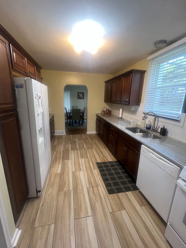 kitchen featuring dark brown cabinetry, a sink, light wood-style floors, white appliances, and arched walkways