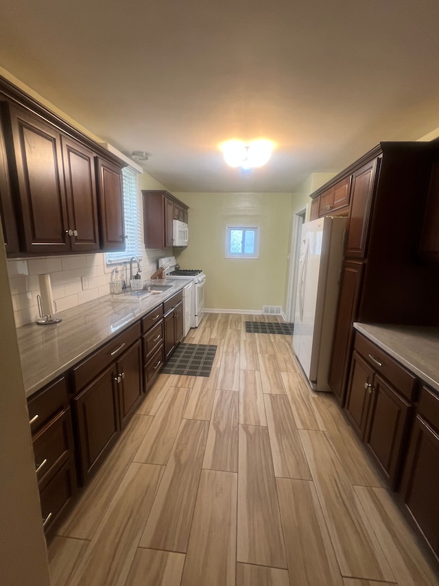 kitchen with a sink, dark brown cabinetry, wood finish floors, and white appliances