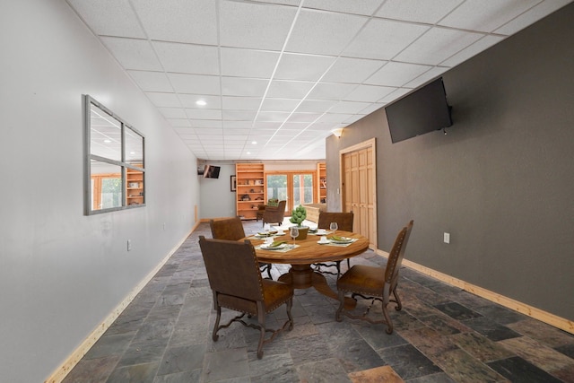 dining room with baseboards, a drop ceiling, and stone finish floor