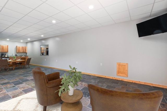 living area featuring baseboards, stone tile floors, a drop ceiling, and recessed lighting