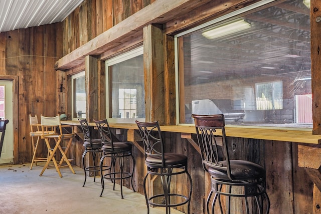 interior space featuring wooden walls, bar, vaulted ceiling, and concrete flooring