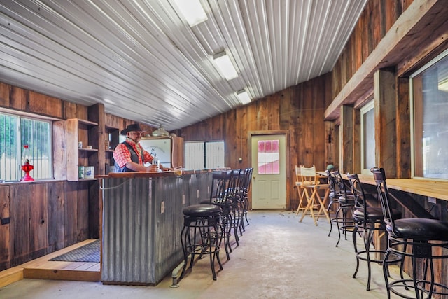 bar with wooden walls, concrete flooring, vaulted ceiling, and a bar