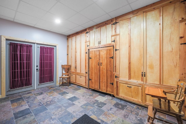 interior space featuring a paneled ceiling, stone finish flooring, and french doors