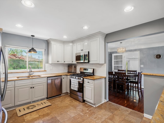 kitchen featuring appliances with stainless steel finishes, a sink, white cabinetry, hanging light fixtures, and light stone finish flooring