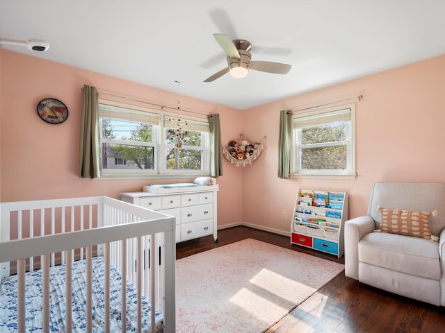 bedroom featuring multiple windows, dark wood-style flooring, a crib, and a ceiling fan