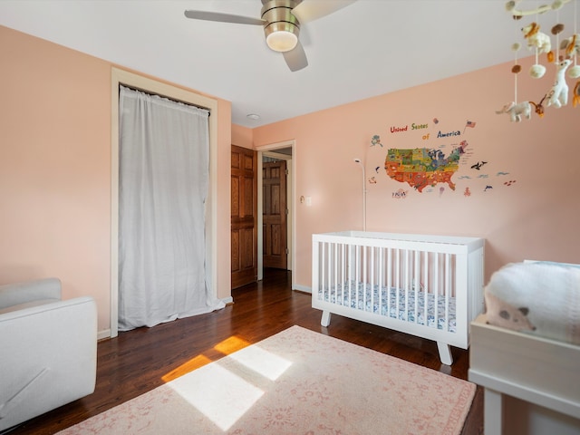 bedroom with wood finished floors, baseboards, a ceiling fan, and a nursery area