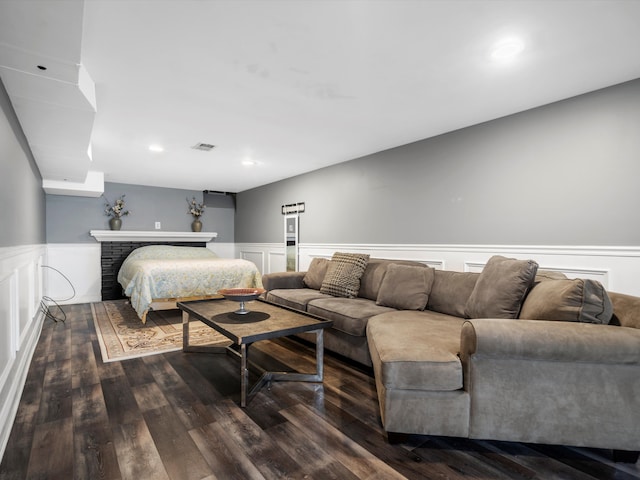 bedroom with a wainscoted wall, dark wood-type flooring, a decorative wall, a brick fireplace, and recessed lighting