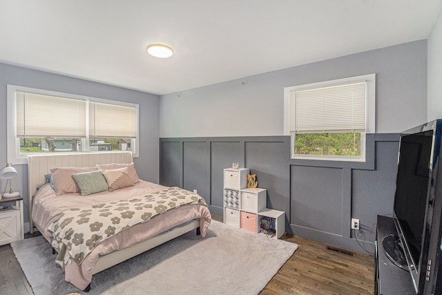 bedroom with visible vents, dark wood-style flooring, wainscoting, and multiple windows