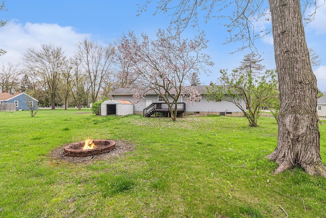 view of yard with a storage unit, a fire pit, an outbuilding, and a deck