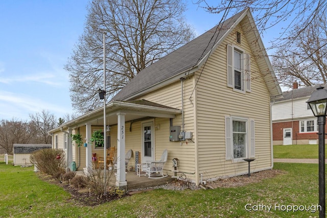 view of front facade with roof with shingles, covered porch, and a front yard