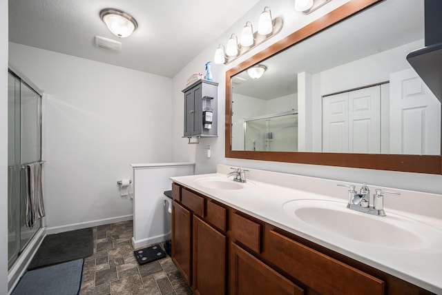 bathroom with baseboards, stone finish flooring, a sink, and a stall shower