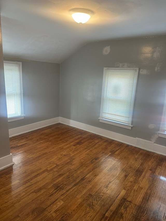 empty room featuring baseboards, visible vents, wood finished floors, and lofted ceiling