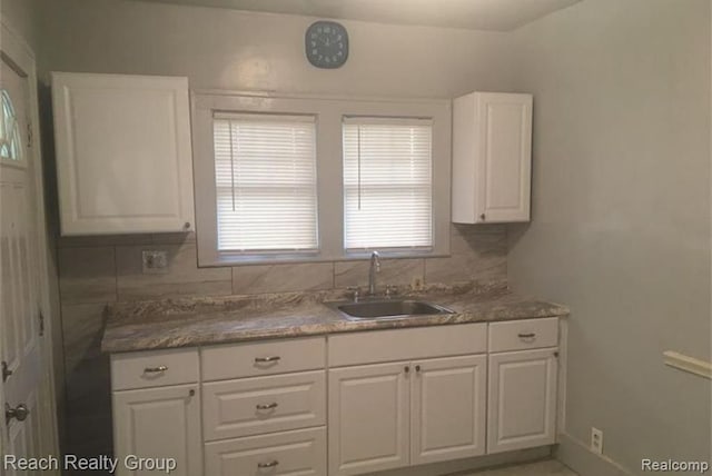 kitchen featuring white cabinetry, baseboards, decorative backsplash, and a sink