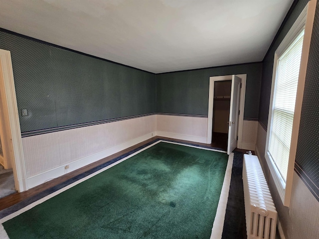 spare room featuring dark colored carpet, wainscoting, and radiator heating unit