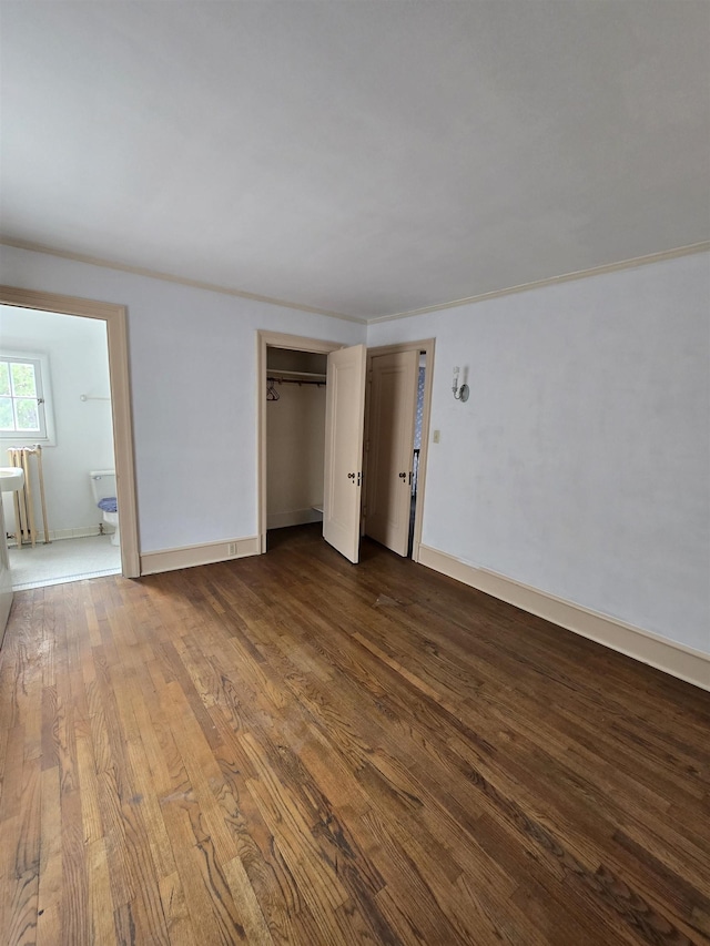 unfurnished bedroom featuring baseboards, ensuite bath, and dark wood-type flooring
