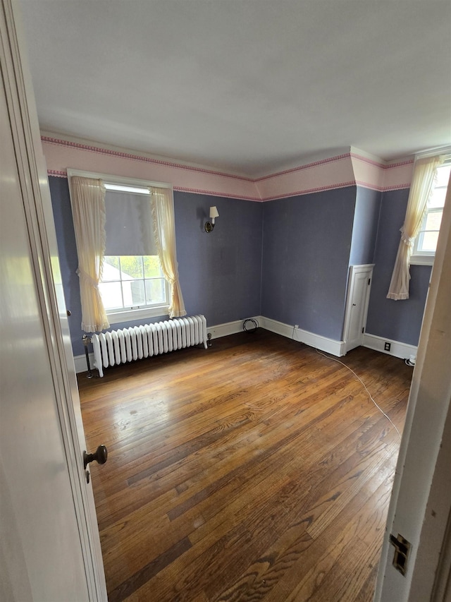 empty room featuring dark wood-type flooring, radiator, and baseboards